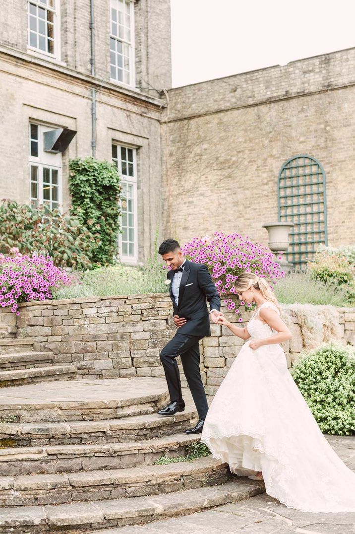 Groom in dark suit and bride in lace dress walking around grounds of Hedsor House