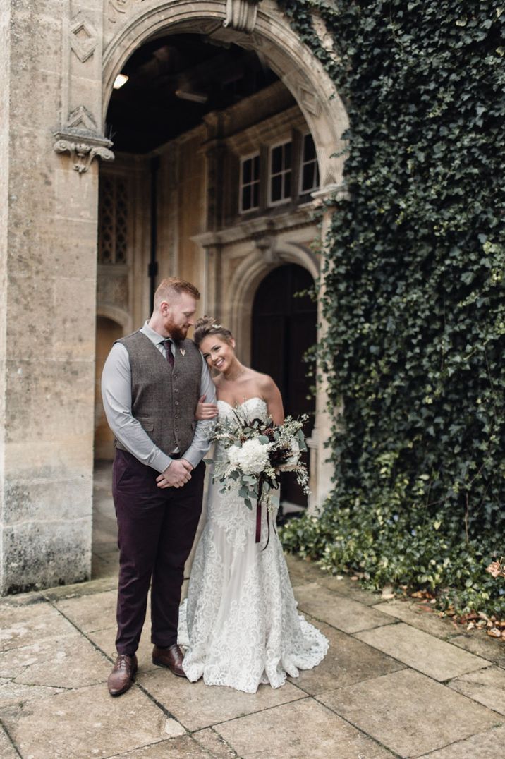 Bride hugs the groom holding a white flower bouquet tied with burgundy ribbon 