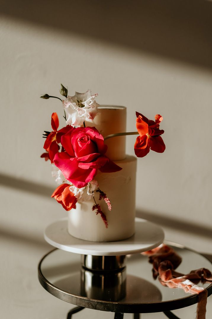 Two tier white frosted wedding cake with bright magenta wedding flowers decorating the cake 