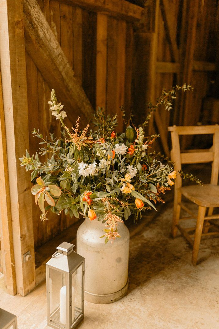 Orange tulips and lots of green foliage in rustic milk churn wedding flower arrangements 