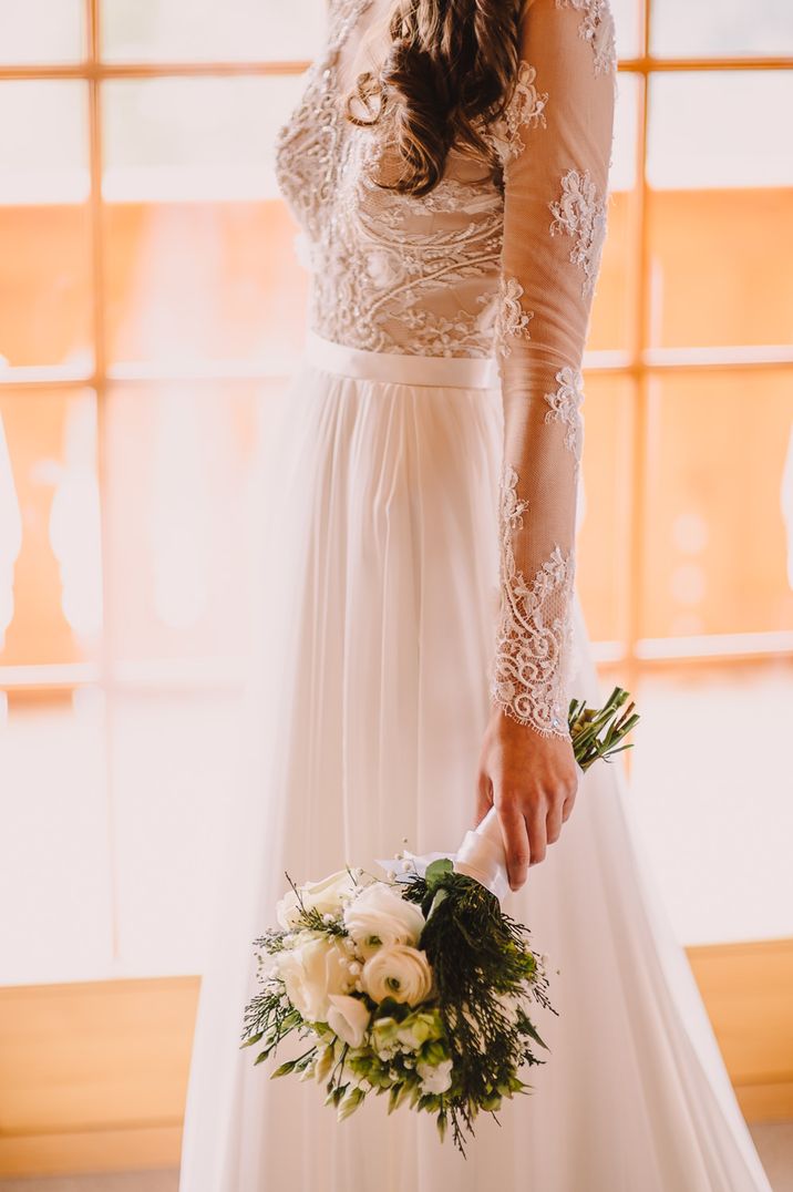 Close up of bride wearing Suzanne Neville Camillia wedding dress and holding bouquet in dropped hand.