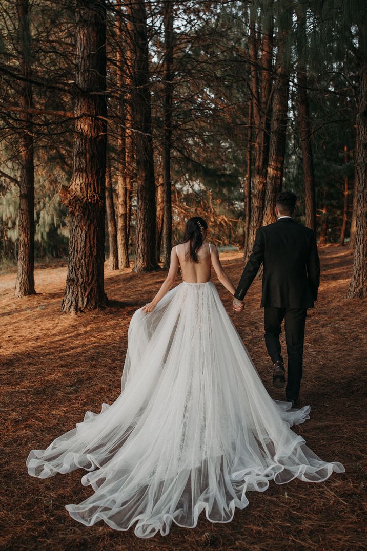 Bride in a fitted lace wedding dress with detachable chiffon shirt talking in the woods with her husband 