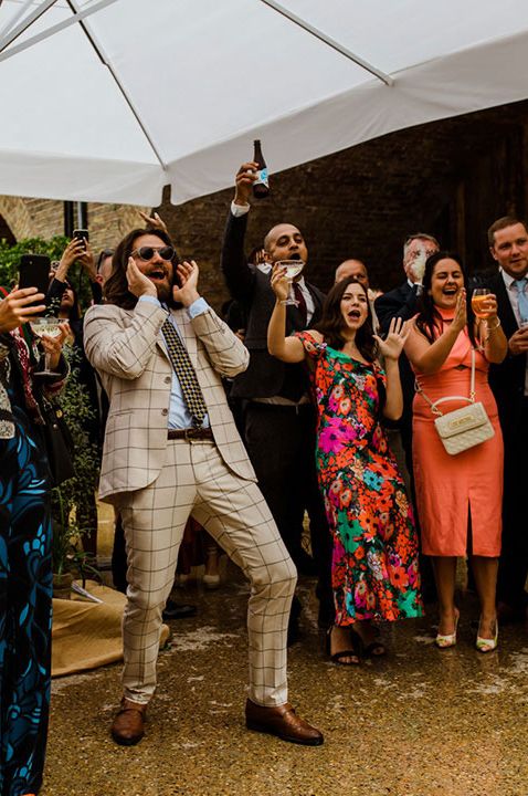 Wedding guests cheering in brightly coloured outfits at maid of honour speech