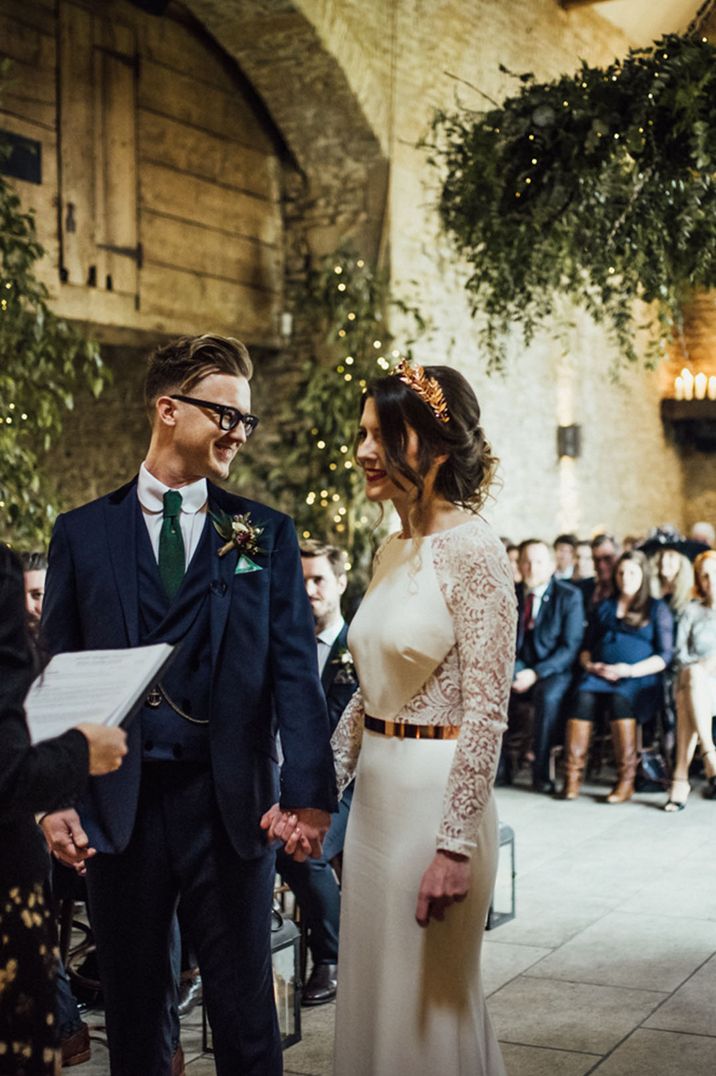 Bride in long sleeve lace wedding dress and golden wedding crown and groom in dark suit at Stone Barn