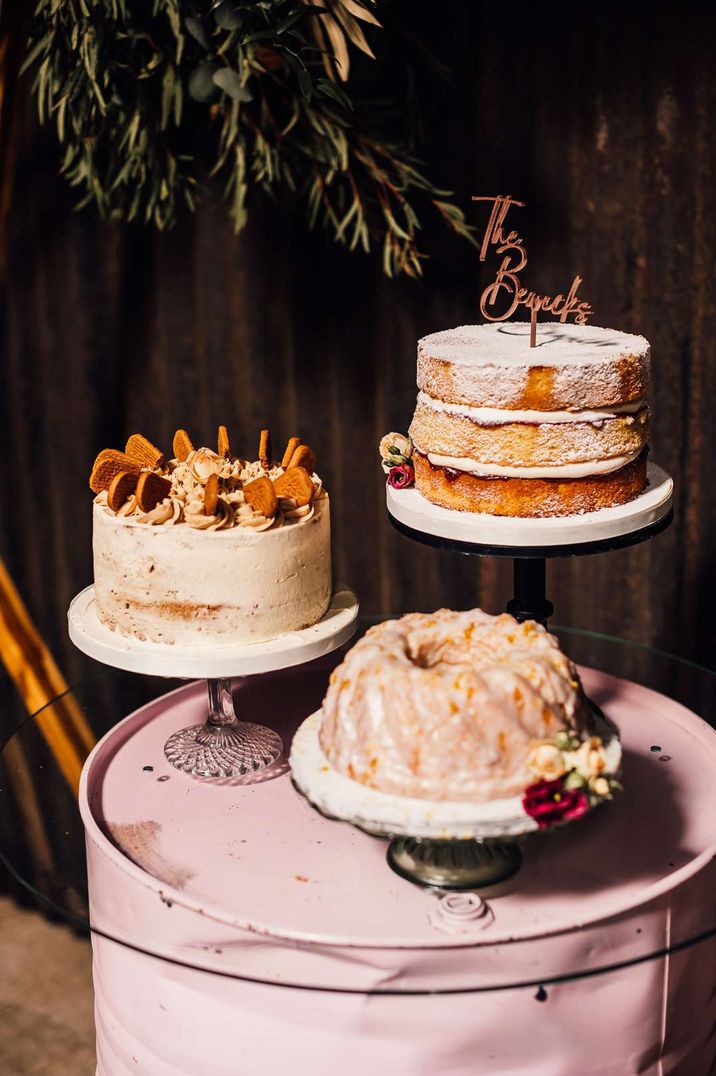 Three wedding cakes on mismatched cake stands next to a hexagonal Moorgate decorated with dried boho flowers at White Skye Fields