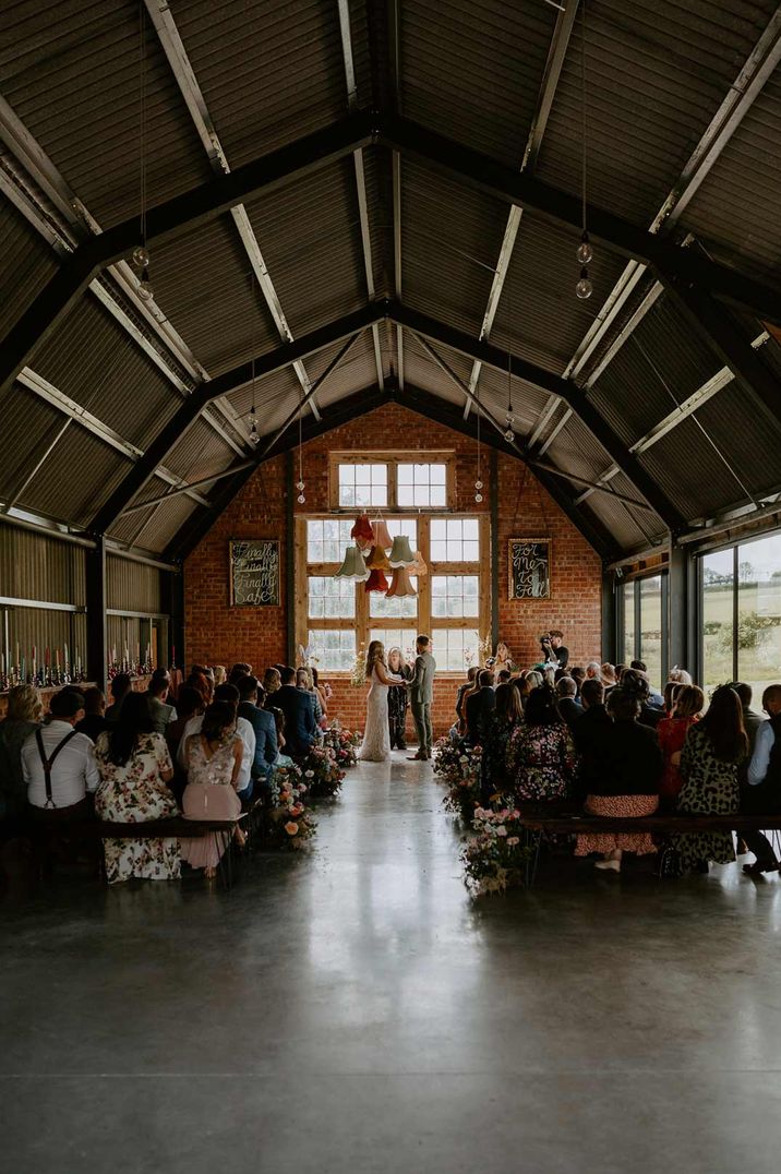 Bride and groom standing at the alter of Giraffe Shed with pastel toned lampshades decorations and a list of questions to ask your wedding venue