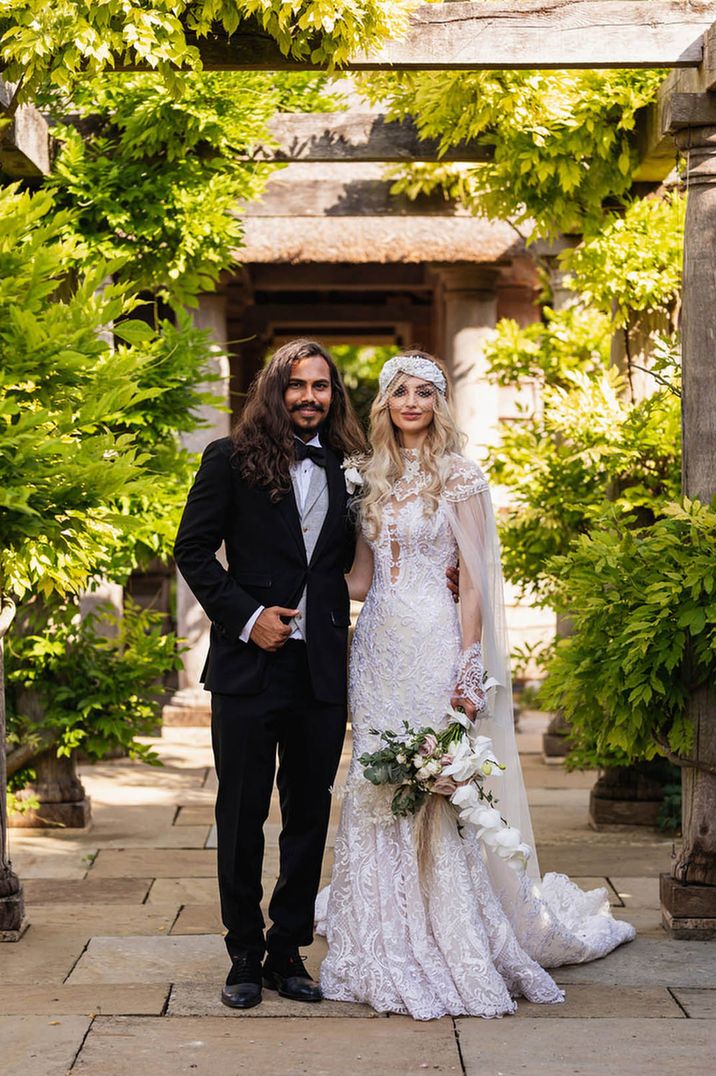 Groom in three piece black tie suit with grey waistcoat and bride in fitted lace wedding dress and bird cage veil 