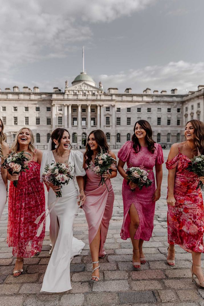 Bride in puff sleeve front leg slit wedding dress walking with bridesmaids in mismatched summery pink bridesmaid dresses 