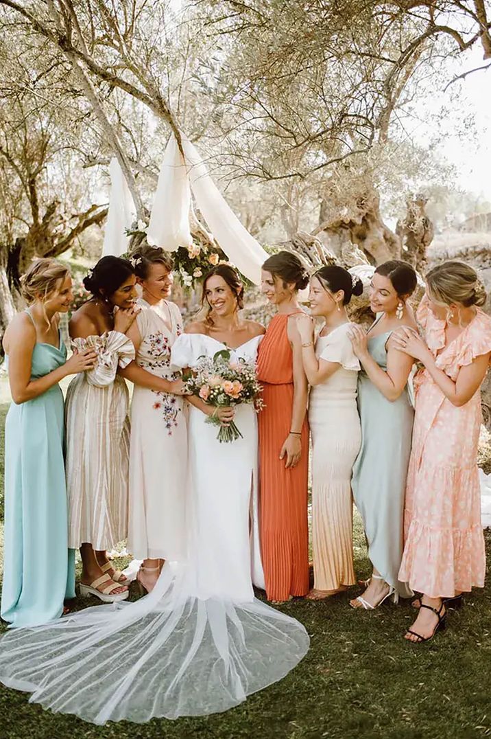 Bride posing with her bridesmaids wearing mismatched, spring-coloured dresses