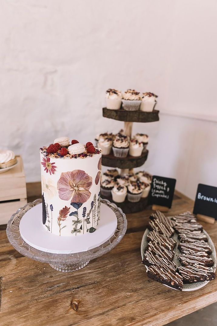 Wildflower pressed wedding cake on a wooden dessert table with brownies and cupcakes 