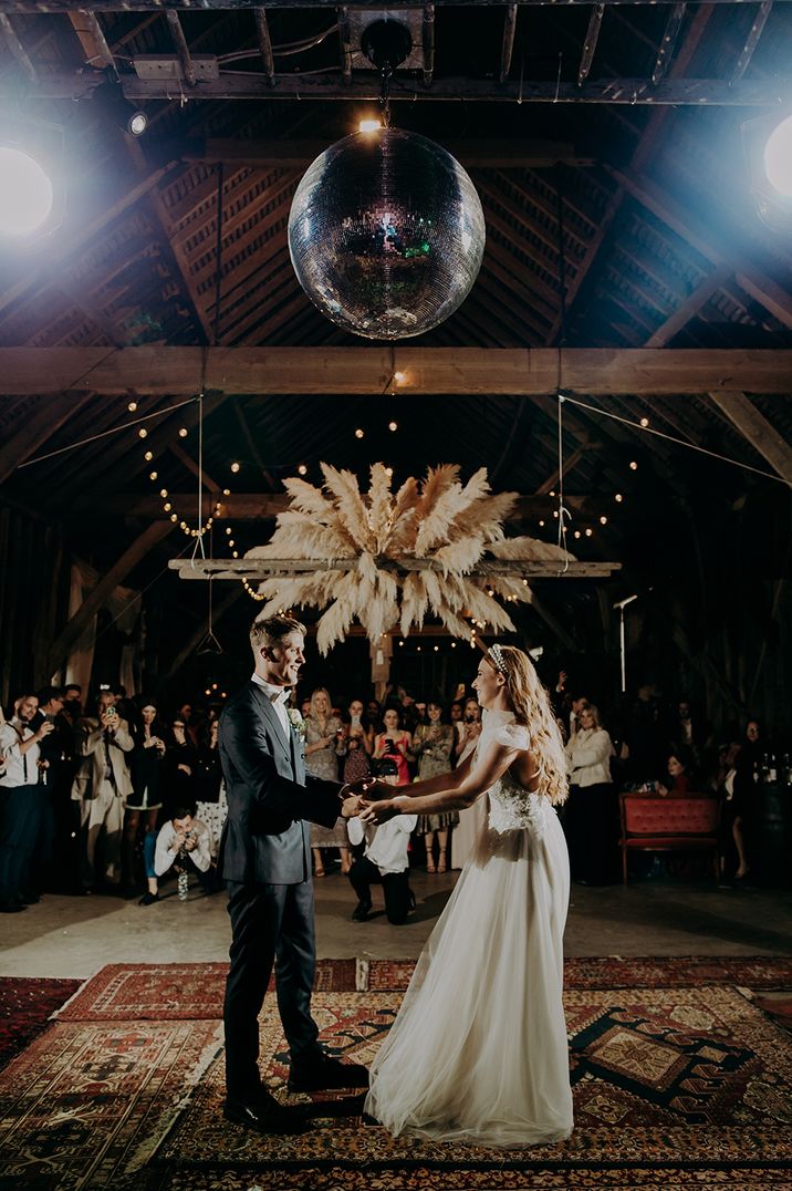 Bride and groom dancing under a giant disco ball and pampas grass installation at boho wedding 