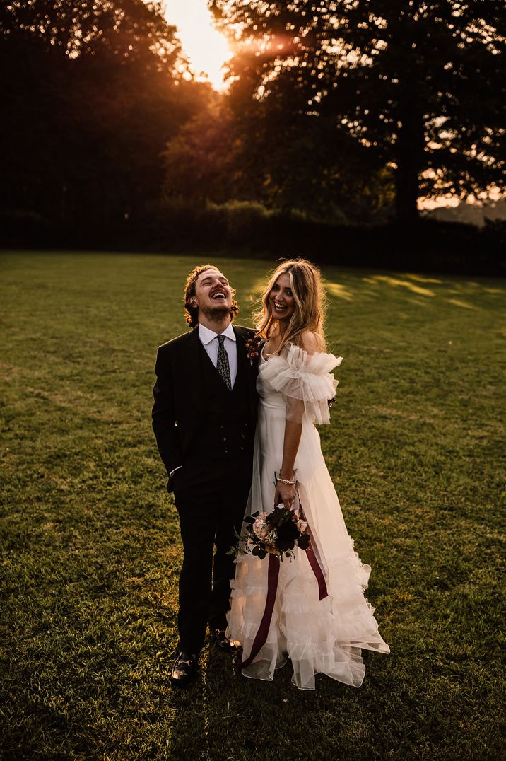 Bride and groom portrait with groom tilting his head back laughing and bride in an of the shoulder ruffle wedding dress