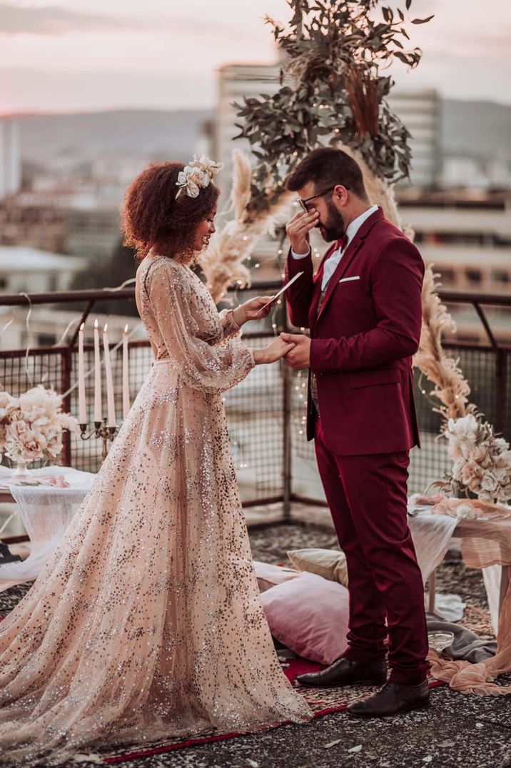 Bride wears long sleeve sparkly wedding dress and floral bridal crown whilst reading her wedding vows outdoors 