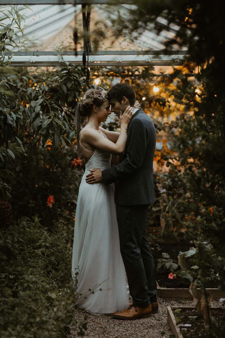 Bride and groom embracing amidst the foliage and exotic florals of The Secret Herb Garden glasshouse wedding venue in Edinburgh 