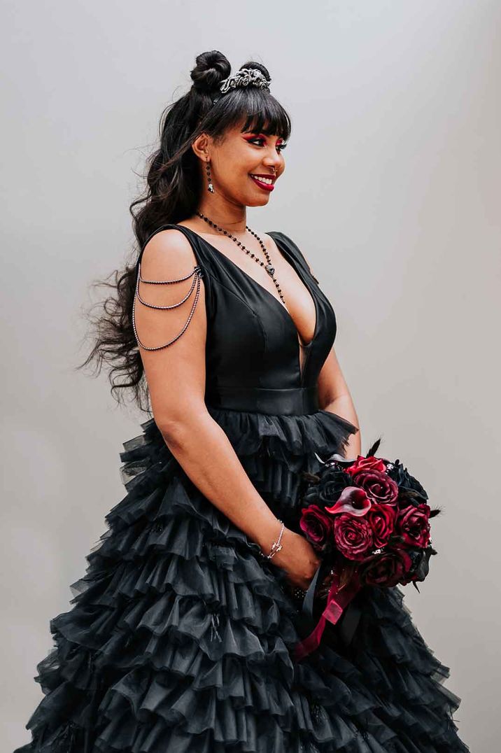 Bride in v neck sleeveless black ruffled wedding dress with black and red rose bouquet 