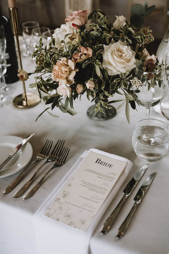 Romantic wedding tablescape with neutral pink florals and a simple white place setting and menu 