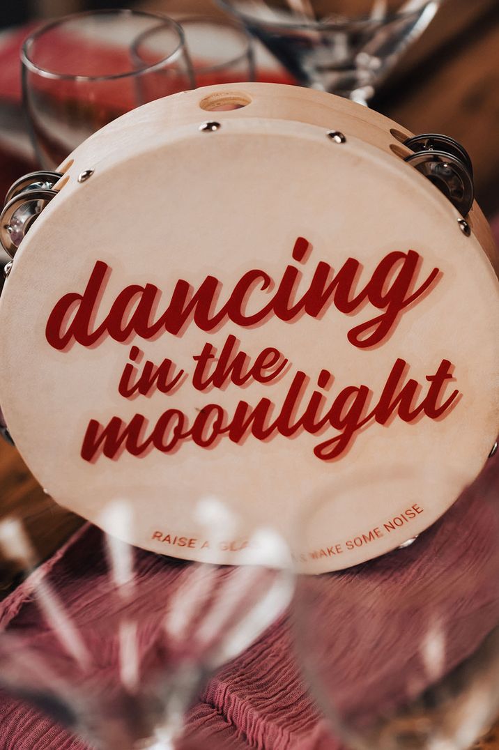 Fun tambourine table names based on disco theme songs to match the festival wedding 