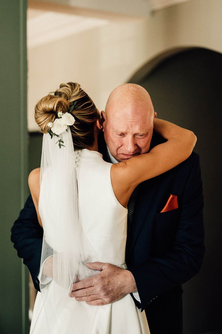 Father of the bride embraces the bride as he sees her in her wedding dress for the first time 