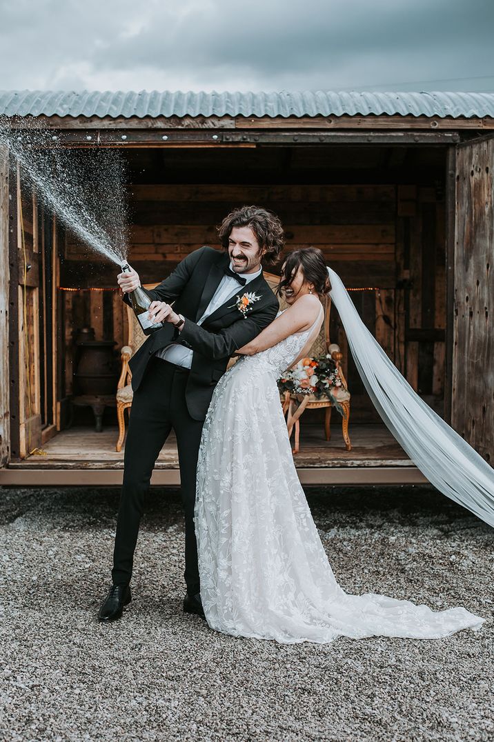 Fun champagne popping photo for the bride and groom at their classic black tie wedding 