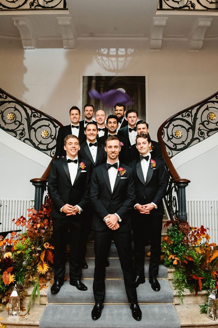 Groom and groomsmen in black tuxedos posing together for group photo