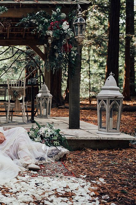 Bride in a strapless wedding dress with flower crown and long veil sitting on the floor in the woods with her husband in a navy blue suit