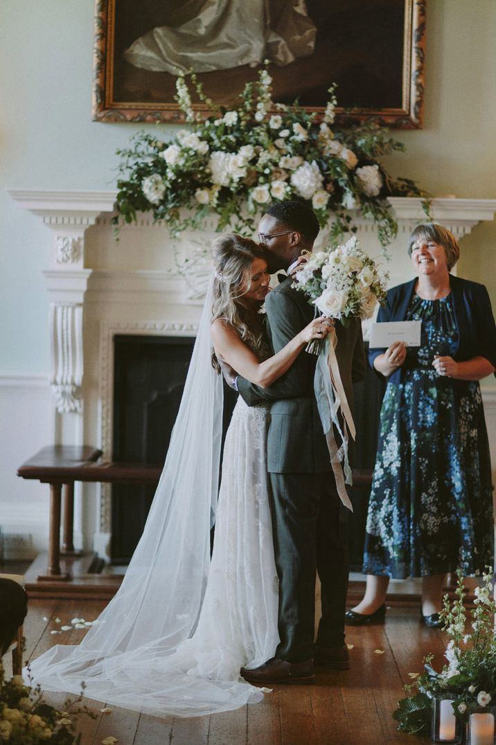 Groom kissing his bride on the head during the wedding ceremony with white and green fireplace flowers 