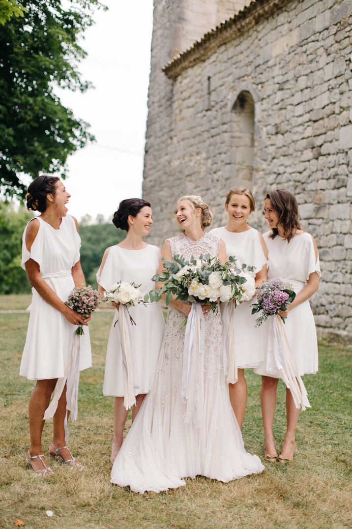 Bridal party wearing short white bridesmaid dresses with open shoulder details