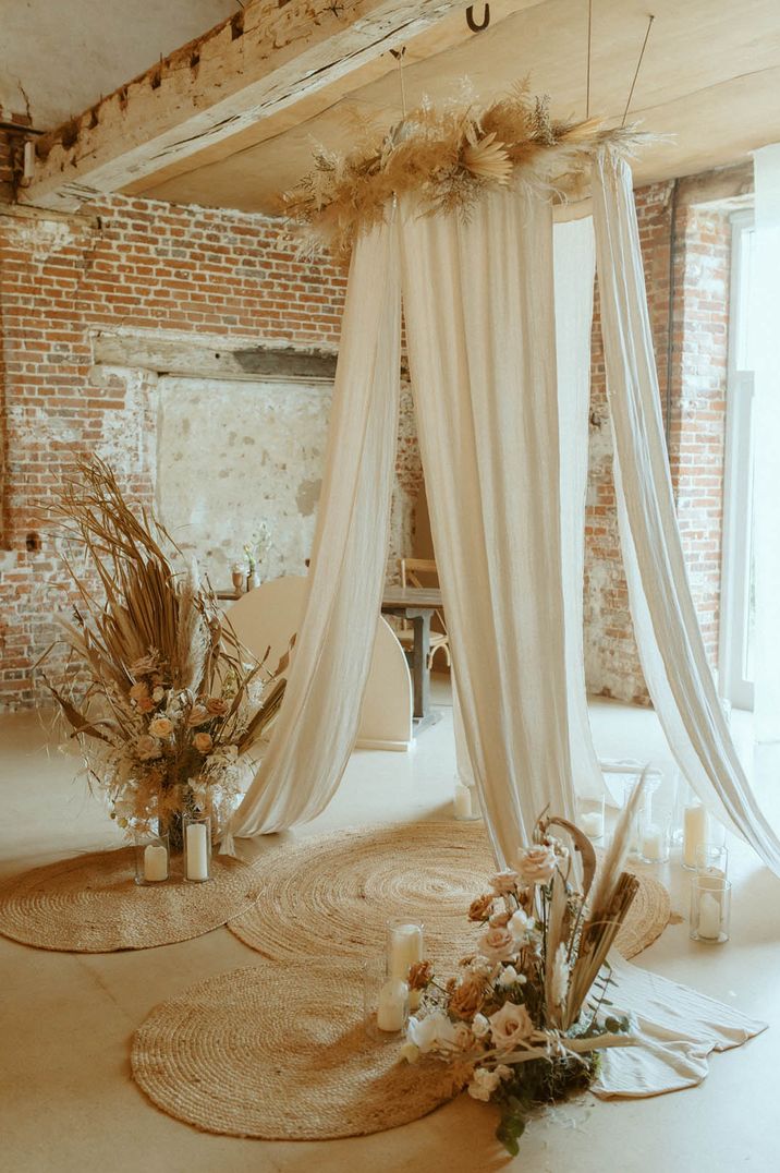 White wedding drapes decorating the altar with boho pampas grass and dried flowers with pillar candles in hurricane vases  