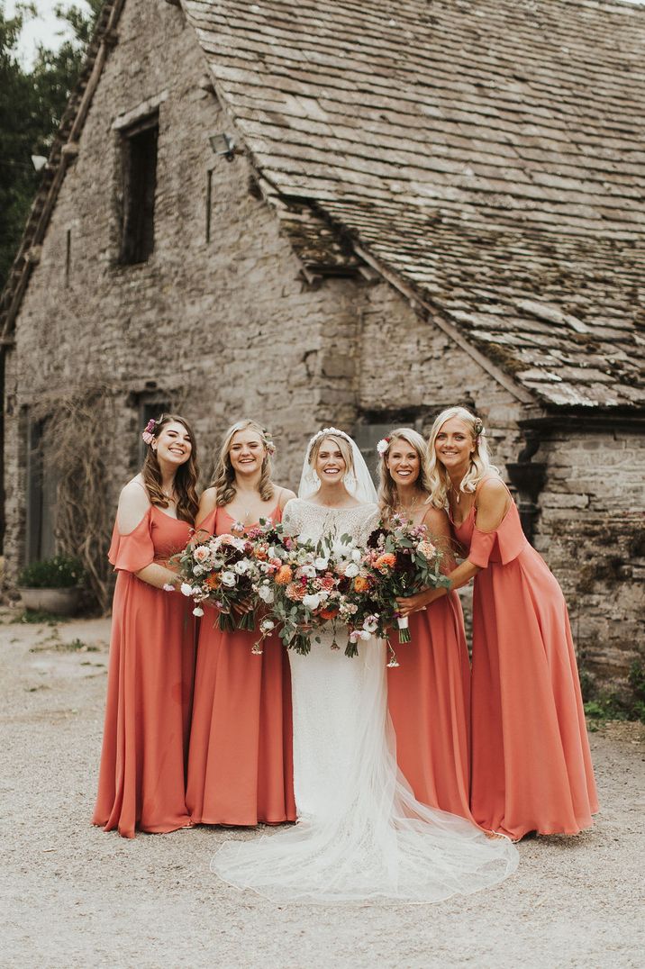 Bride standing with bridal party in coral bridesmaid dresses with open shoulder details