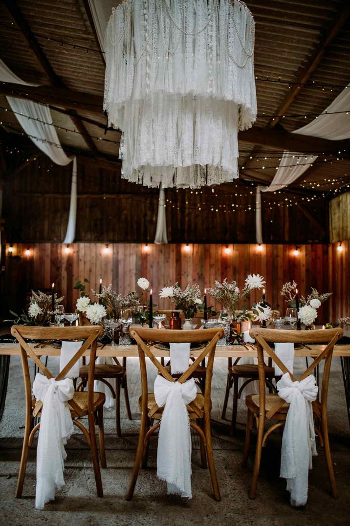 Rustic luxury wedding tablescape with white drapery over the chandelier, white tulle ribbons on the backs of the chairs, fairy lights and white floral centrepieces - wedding budget spreadsheet 