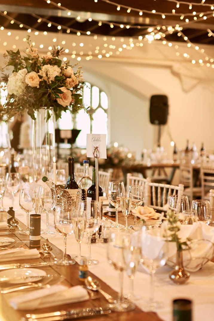 Classic wedding tablescape at Cluny Castle wedding venue - white table runner, garden rose, peony and foliage centrepieces, tapered candles, and gold cutlery with fairy lights hanging above 