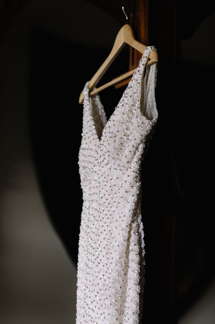 Embellished beaded wedding dresses hanging on wooden hanger by Rebecca Goddard Photography