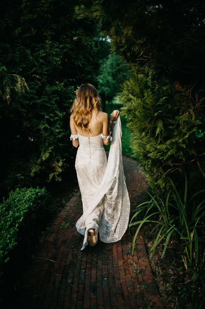 Boho bride in a strapless Rue De Seine wedding dress holding up her train as she walks through the woods