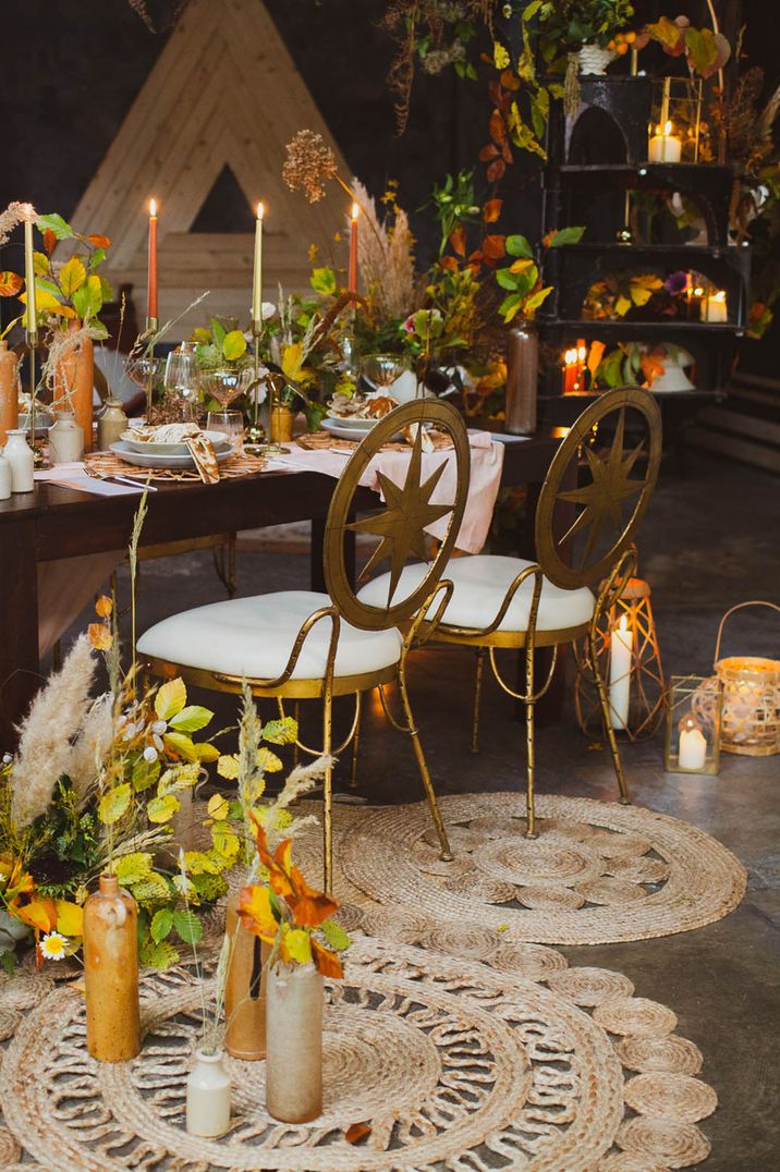 Autumnal style tablescape with gold chairs, woven mats, orange and green leaves and candles with wooden candle lanterns by The Boho Shack