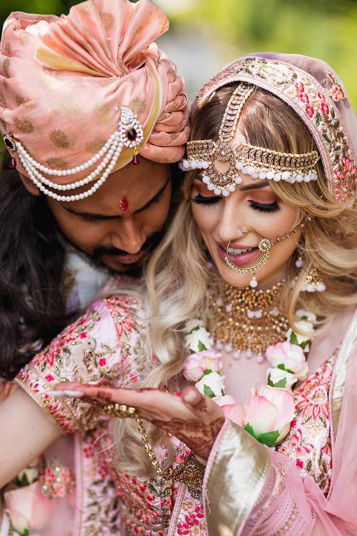 Bride wearing gold and pink bead jewellery with pink outfit and headdress with the groom in pink outfit for Hindu multicultural wedding 