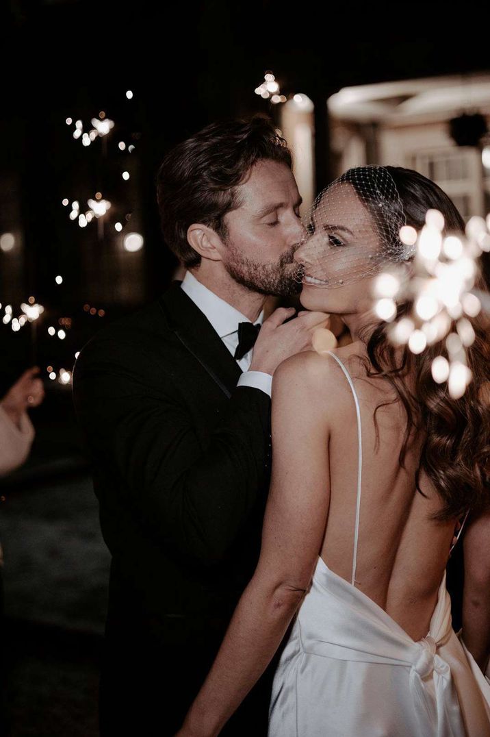 Bride in birdcage wedding veil and low back satin strappy wedding dress doing sparkler exit with groom in black tux at Eaves Hall Clitheroe wedding venue 