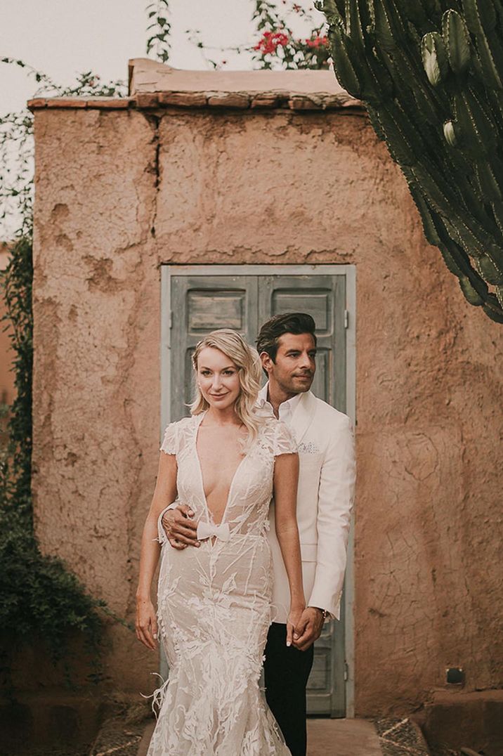 Bride in plunging wedding dress with bow detail standing with groom in white jacket at exotic destination wedding 