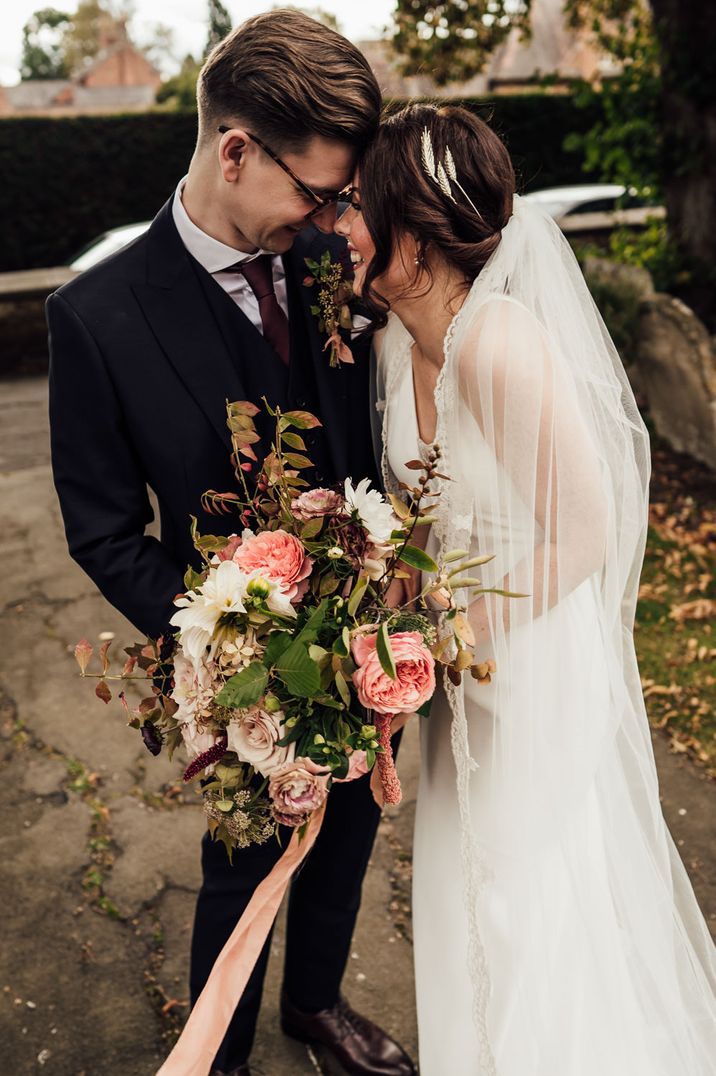 Bride and groom portrait with bride in a lace edged veil holding and autumn wedding bouquet 