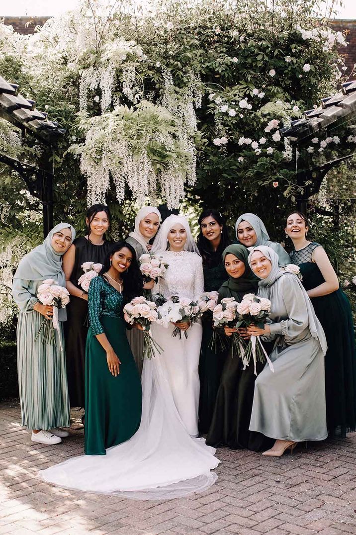 Bridesmaids in light and dark green bridesmaid dresses with some wearing matching hijabs with bride in high neck long sleeve lace wedding dress 