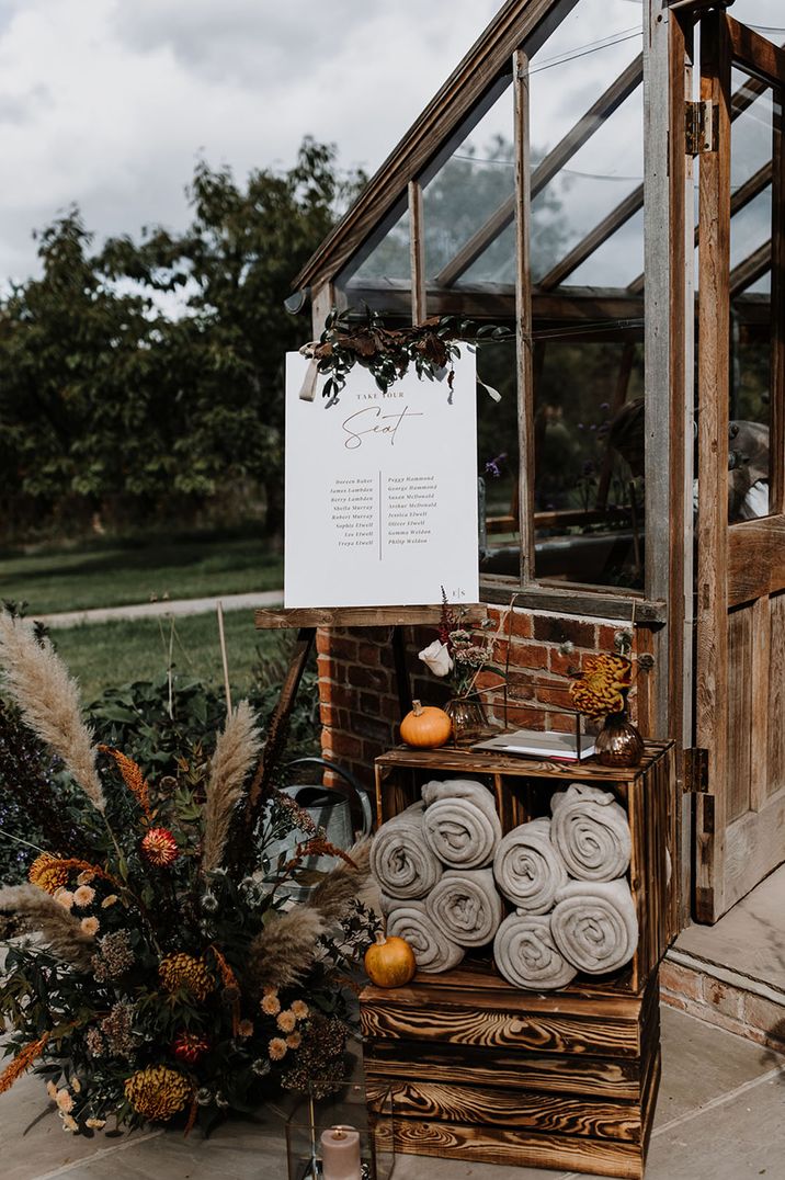 Wooden crates full of grey fluffy blankets under the table plan sign for winter wedding decor 