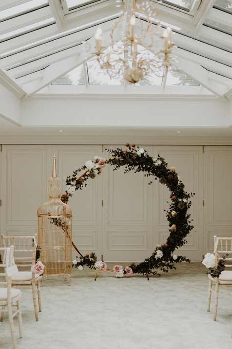 Reception room at Hayne House wedding venue with large wooden circular arch with white rose and foliage decorations - questions to ask your wedding venue