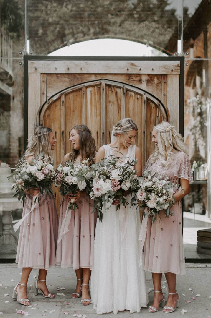 Bridal party wearing soft pastel pink embellished bridesmaid dresses with the bride holding pink and white rose bouquets 