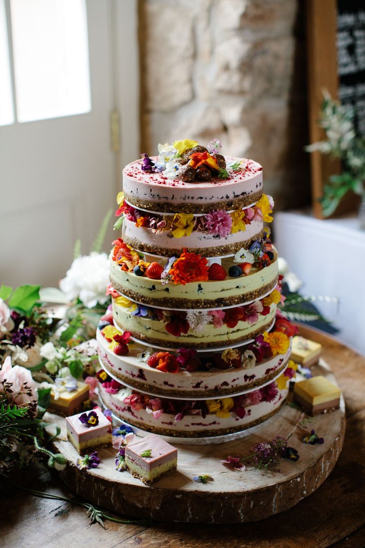 Naked cake decorated with summer fruits like strawberries, blueberries and colourful edible flowers 