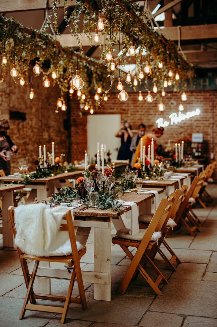 Intimate rustic wedding reception with wooden tables, Edison build installation, candles and orange flowers 