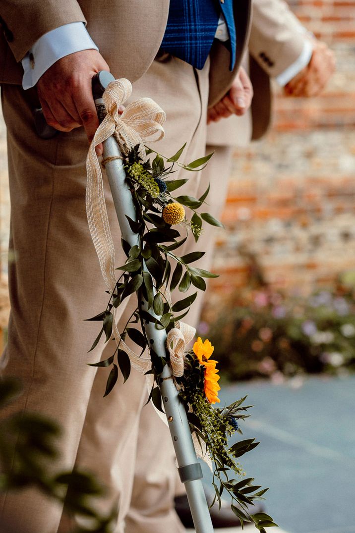 groom in a beige suit holding his walking stick decorated with vines and billy bobs