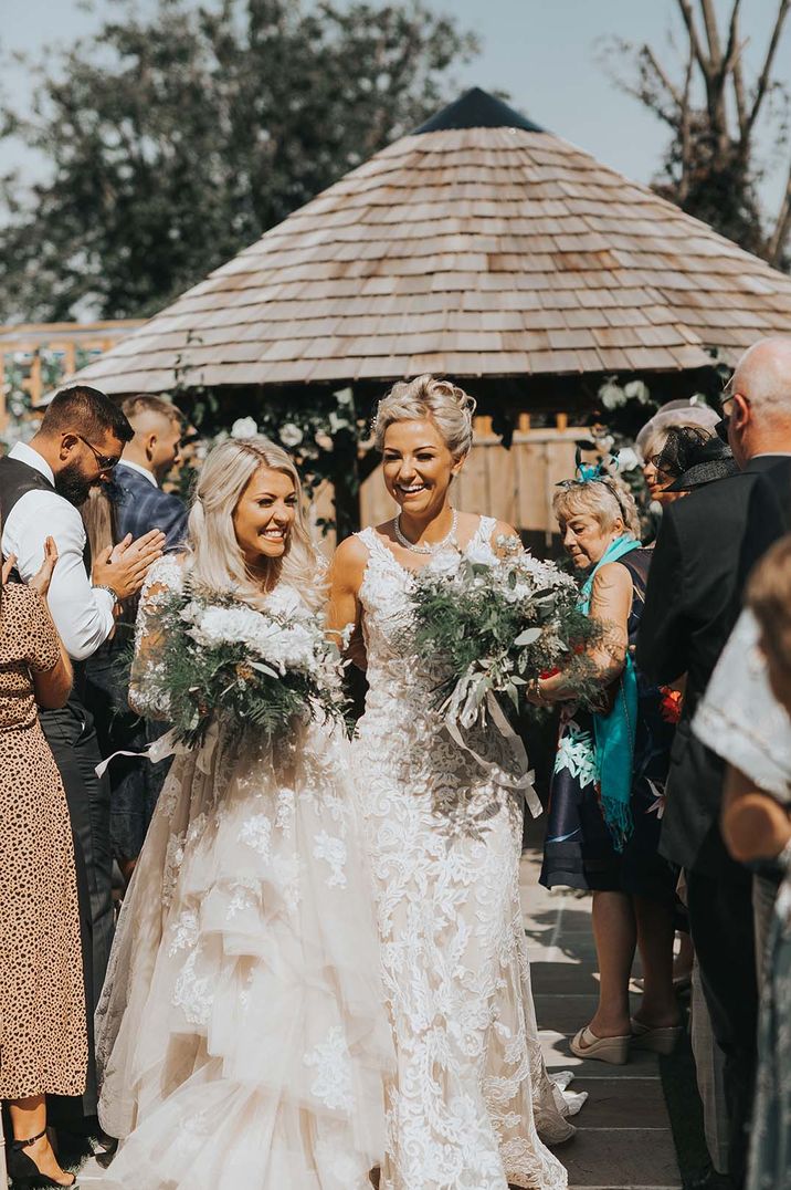 Newlyweds exit their outdoor LGBTQI+ wedding ceremony smiling and laughing