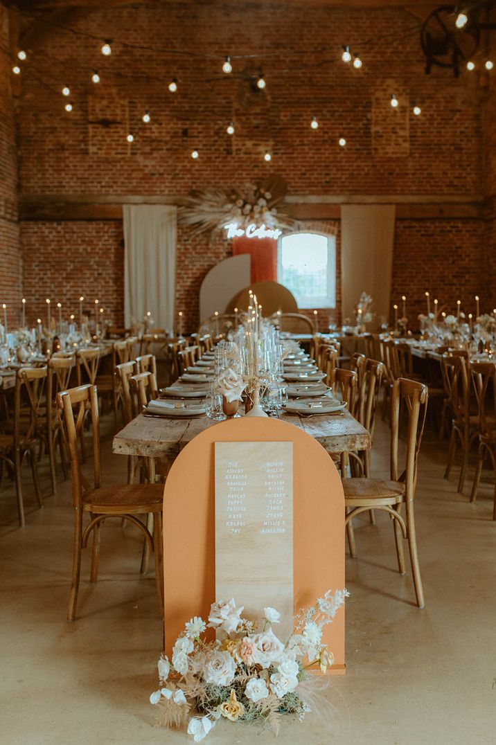 Boho luxe wedding tablescape with orange and light wood mini seating charts at the end of each table and neon sign