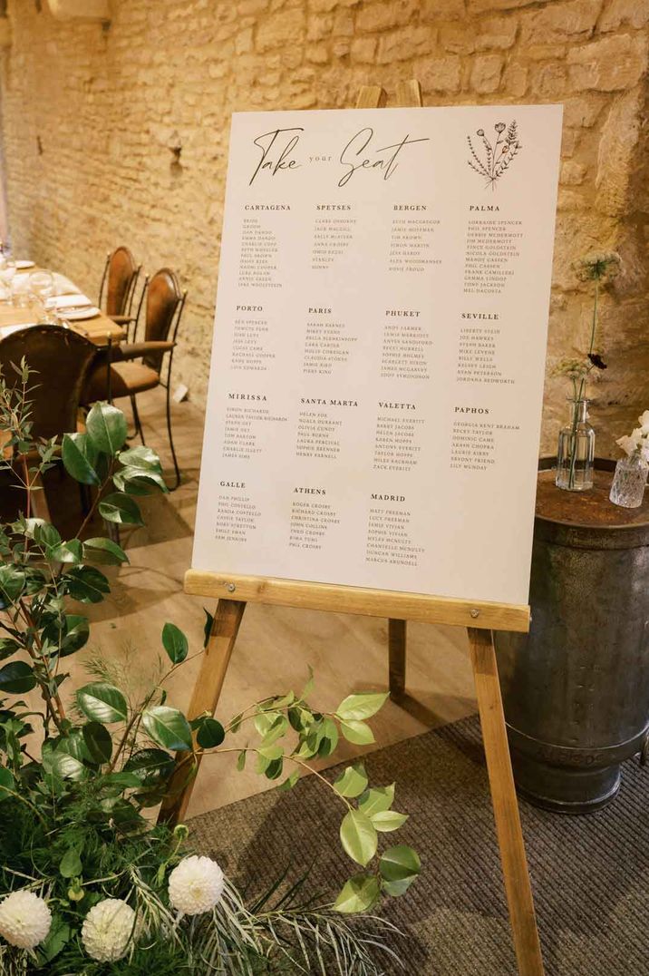 Minimalistic wedding table plan on wooden easel by foliage and peony floral arrangement at The Tythe Barn wedding venue search 