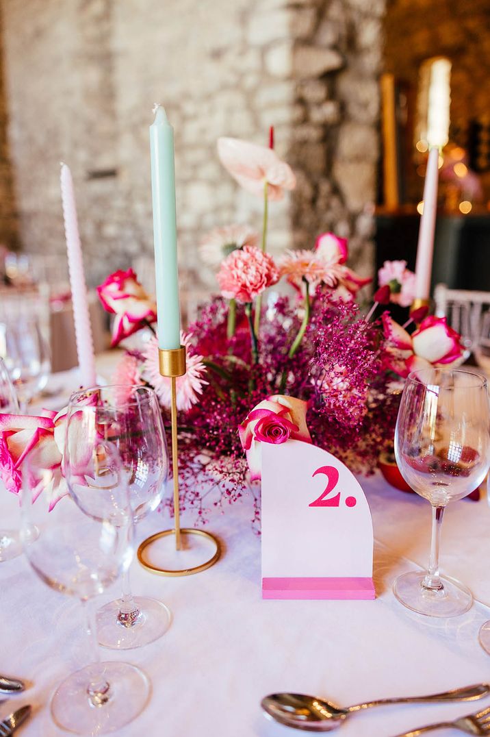 Bright pink theme wedding with retro table number sign and pink floral arrangement with turquoise taper candles 