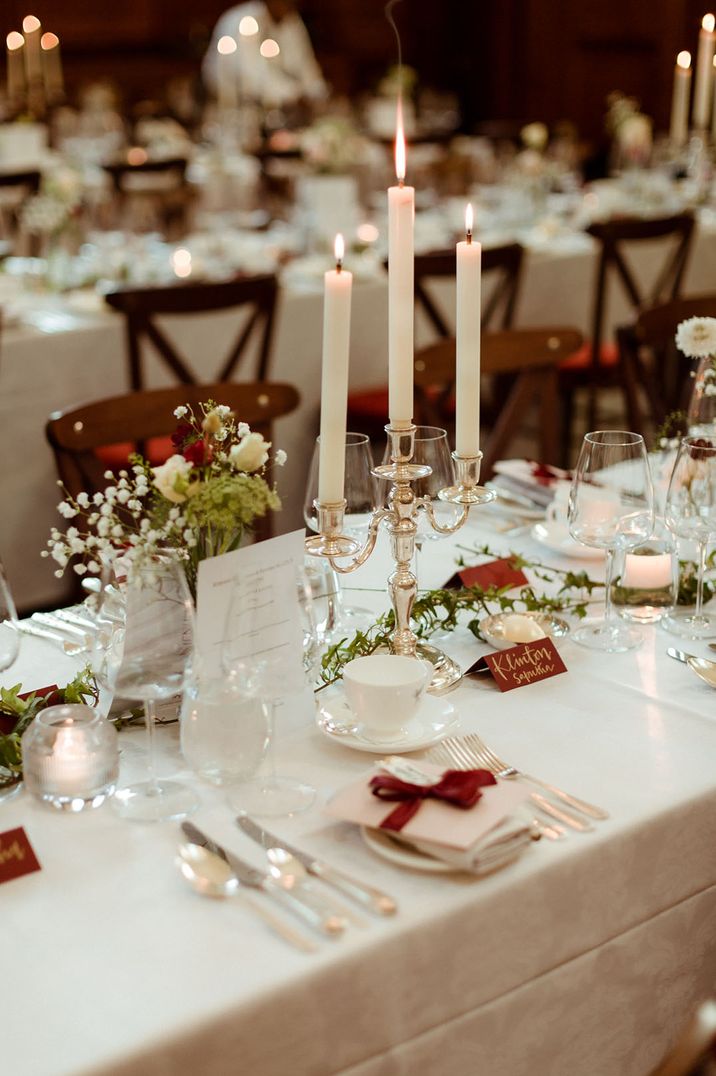 Simple minimalist white and green wedding tablescape with red ribbon wrapped around the plates and menus like a Christmas present 